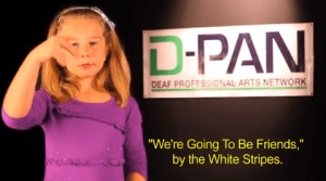 Image description: photograph of young girl with blond hair and light skin, She is using American Sign Language. In the background a large white rectangular sign reads D-PAN, Deaf Professional Arts Network. Closed Captioning in Yellow at bottom of image reads" We're Going To Be Friends , " by the White Stripes.