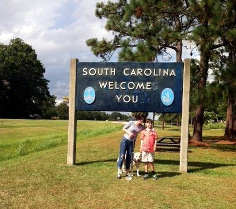 South Carolina Welcomes You road side sign, woman, boy and dog stand underneath