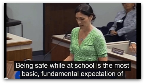 Image Description: Photograph of woman with white skin and brown hair looking down while standing at a podium. She is wearing a green dress. The words "Being safe while at school is the most basic, fundamental expectation of"