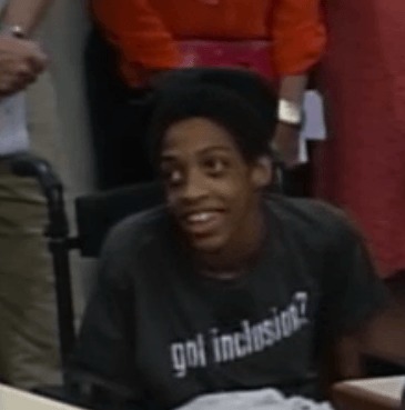 Teenager with brown skin and dark brown hair smiling and wearing a "got inclusion" t-shirt.